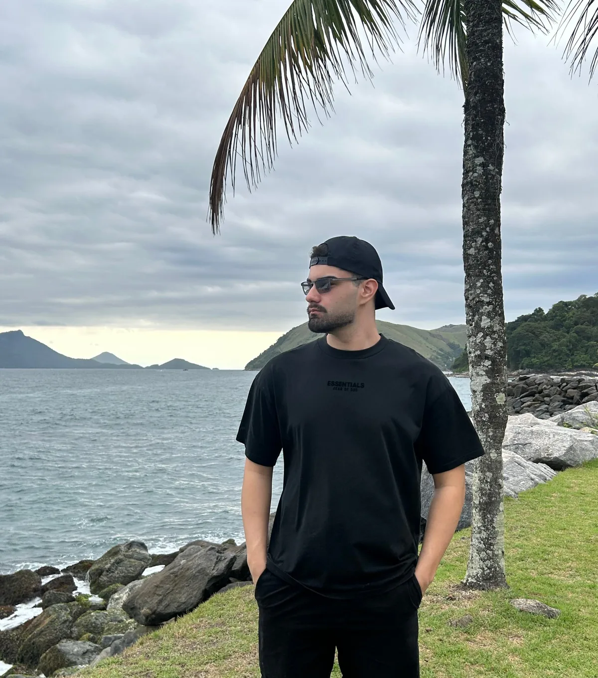 William Soares by the sea, wearing a black cap and sunglasses